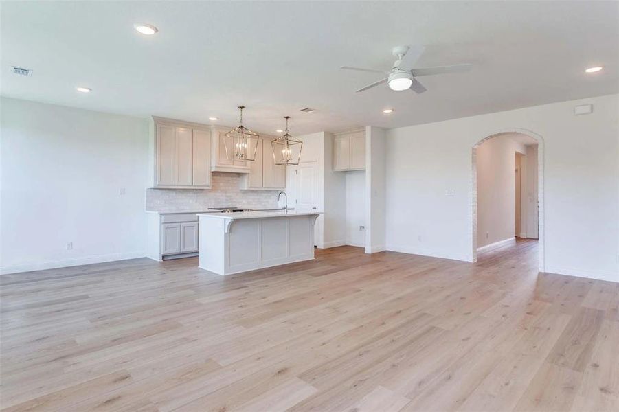 Kitchen with backsplash, open floor plan, arched walkways, pendant lighting, and light wood-type flooring