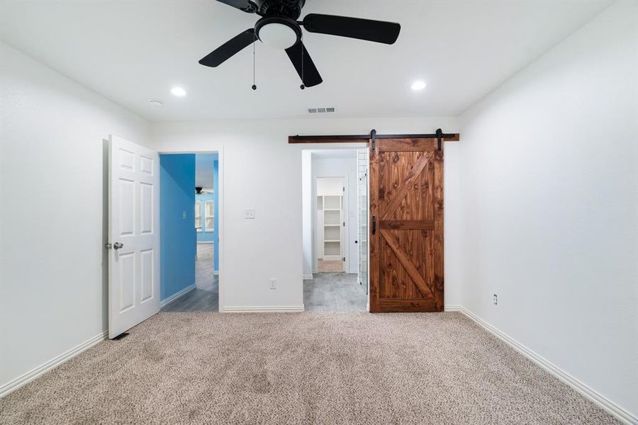 Unfurnished bedroom with a barn door, a spacious closet, carpet, a ceiling fan, and recessed lighting Unfurnished bedroom with a barn door, a spacious closet, carpet, a ceiling fan, and recessed lighting