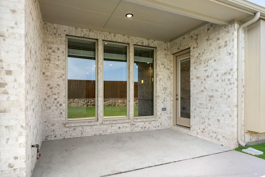 Covered back patio with concrete floor, light brick exterior, large windows, and a back door Covered back patio with concrete floor, light brick exterior, large windows, and a back door