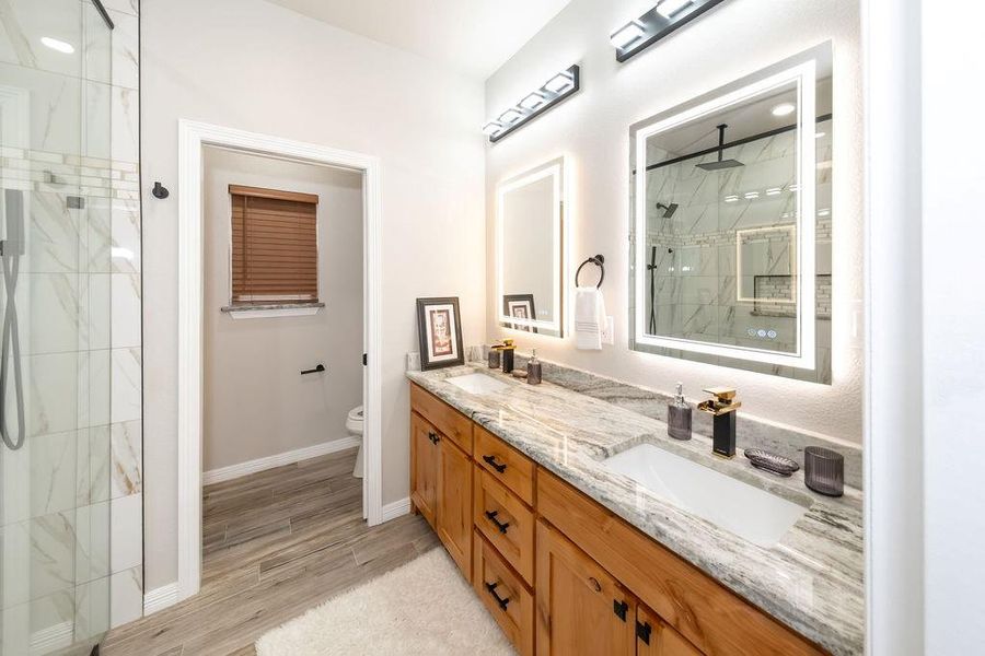 Bathroom with wood-type flooring, tiled shower, vanity, and toilet