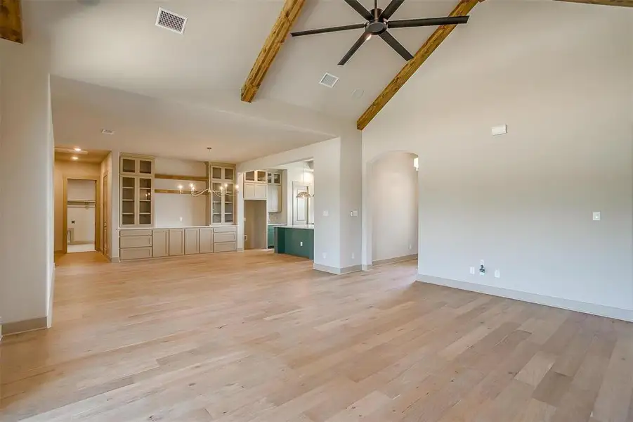 Unfurnished living room featuring arched walkways, high vaulted ceiling, ceiling fan with notable chandelier, and visible vents