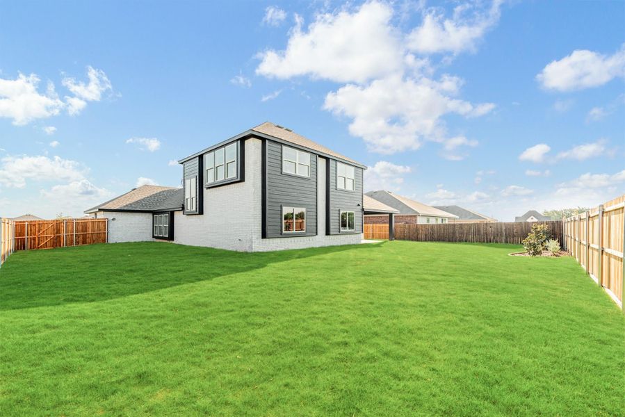 Two-story home with gray siding and brick exterior, large fenced backyard with green lawn