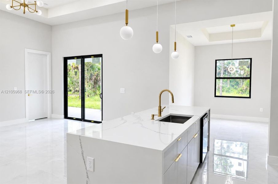 Kitchen island featuring a waterfall-edge countertop, undermount sink with a brass faucet, contemporary pendant lighting, light-tone cabinetry with gold-finish hardware, and large-format tile flooring