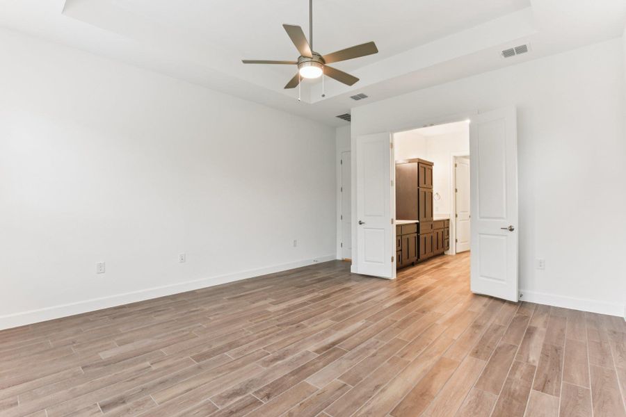 Empty room with a raised ceiling, wood finish floors, and a ceiling fan Empty room with a raised ceiling, wood finish floors, and a ceiling fan