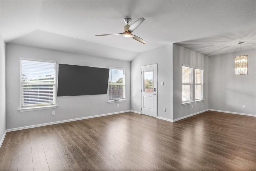 Unfurnished living room featuring ceiling fan with notable chandelier, dark wood-type flooring, and vaulted ceiling