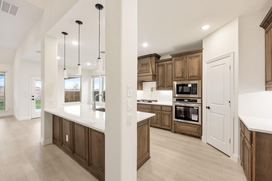 Kitchen with dark wood cabinets, white countertops, stainless steel appliances, and pendant lights over large island Kitchen with dark wood cabinets, white countertops, stainless steel appliances, and pendant lights over large island