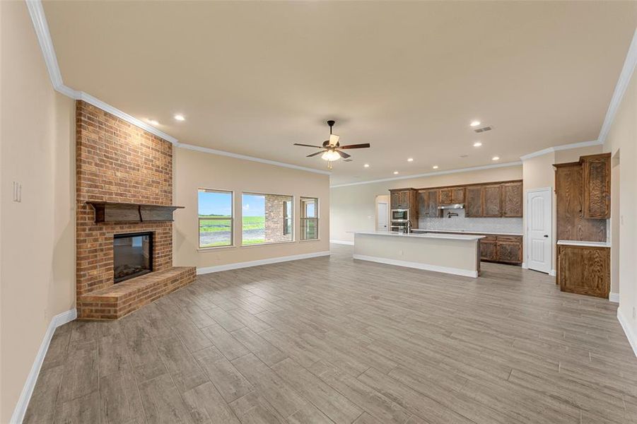 Unfurnished living room featuring a ceiling fan, a fireplace, light wood-style flooring, recessed lighting, and crown molding