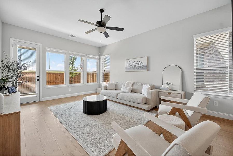 Bright living space featuring light wood-finish flooring, a contemporary ceiling fan, and multiple windows