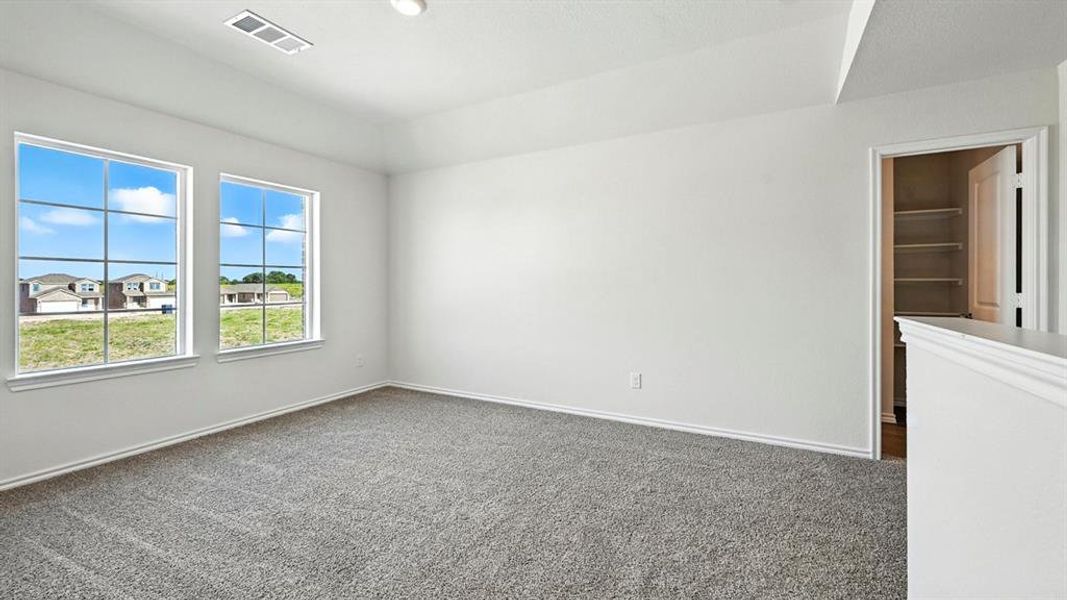 Spacious room featuring neutral carpeting, white walls, two large windows with grid patterns, a tray ceiling, and an open doorway revealing built-in shelving