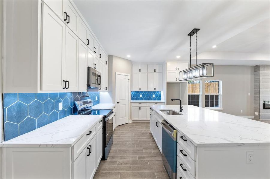 Kitchen featuring pendant lighting, an island with sink, sink, white cabinets, and stainless steel appliances