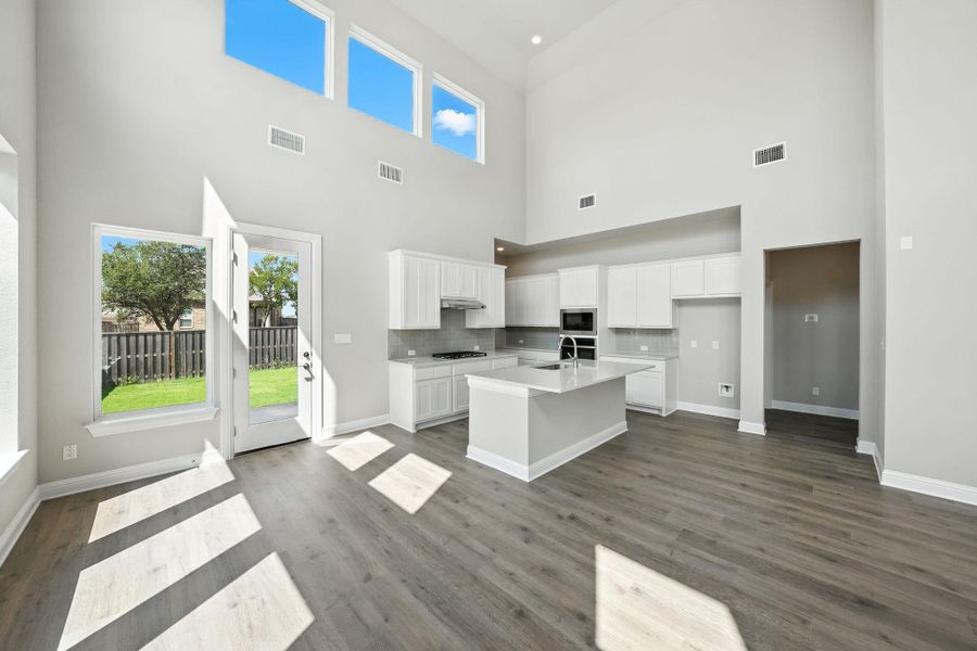 Kitchen with white cabinetry, a kitchen island with sink, decorative backsplash, dark wood-type flooring, and a towering ceiling Kitchen with white cabinetry, a kitchen island with sink, decorative backsplash, dark wood-type flooring, and a towering ceiling