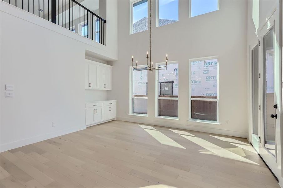 Unfurnished living room featuring a towering ceiling, an inviting chandelier, and light wood-type flooring