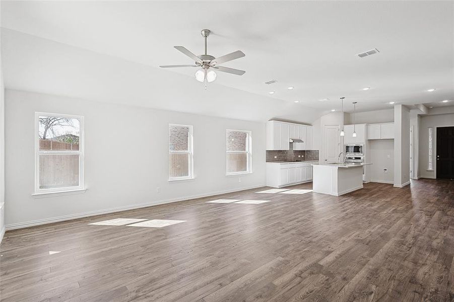 Unfurnished living room featuring ceiling fan, sink, wood-type flooring, and vaulted ceiling