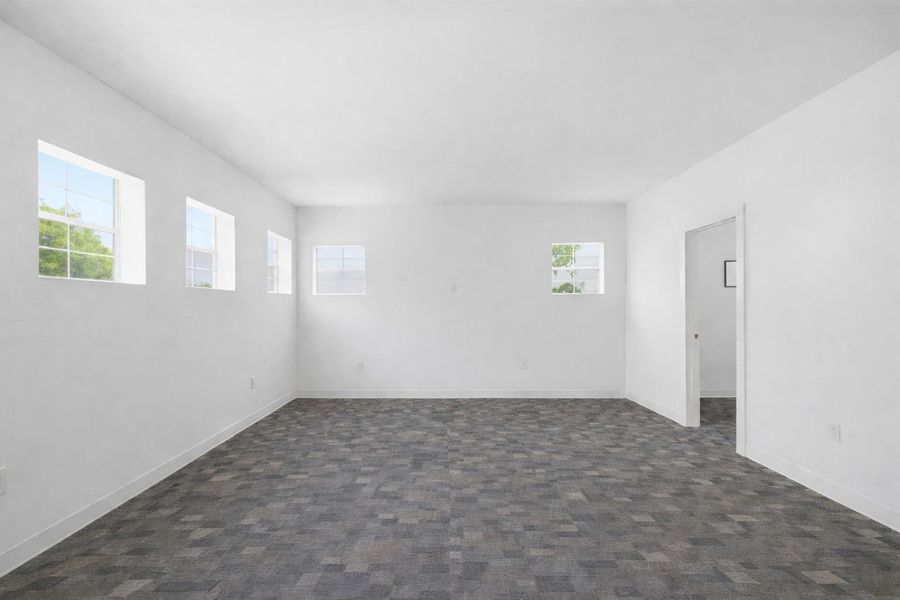 Spacious room with a patterned carpet, white walls, and multiple windows providing natural light