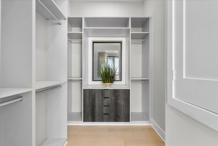 This photo showcases a modern walk-in closet with ample storage space, featuring open shelving, hanging rods, and a central drawer unit. A decorative plant adds a touch of greenery, and the light wood flooring complements the clean, minimalist design. This photo showcases a modern walk-in closet with ample storage space, featuring open shelving, hanging rods, and a central drawer unit. A decorative plant adds a touch of greenery, and the light wood flooring complements the clean, minimalist design.