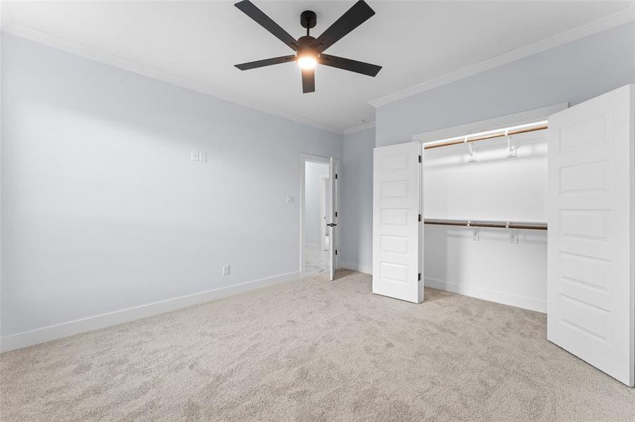 Unfurnished bedroom featuring a closet, ceiling fan, light colored carpet, and ornamental molding