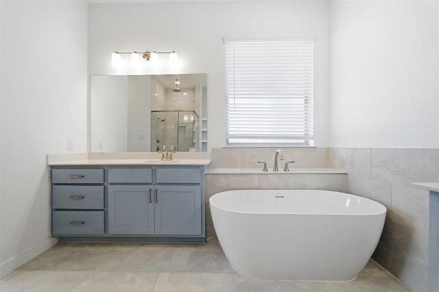 Freestanding soaking tub with a brushed nickel faucet, light blue vanity with a light-toned countertop, and a glass-enclosed shower with a rainfall showerhead