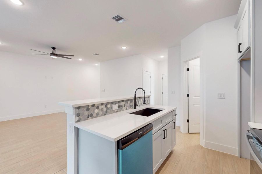 Kitchen featuring an island with sink, light wood-style flooring, dishwashing machine, stainless steel range oven, and a ceiling fan