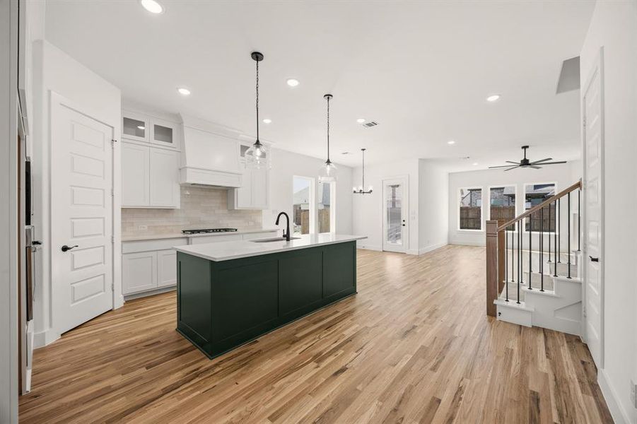Dual tone kitchen featuring a center island with sink, two tone color scheme, a ceiling fan, light wood-style floors, and tasteful backsplash