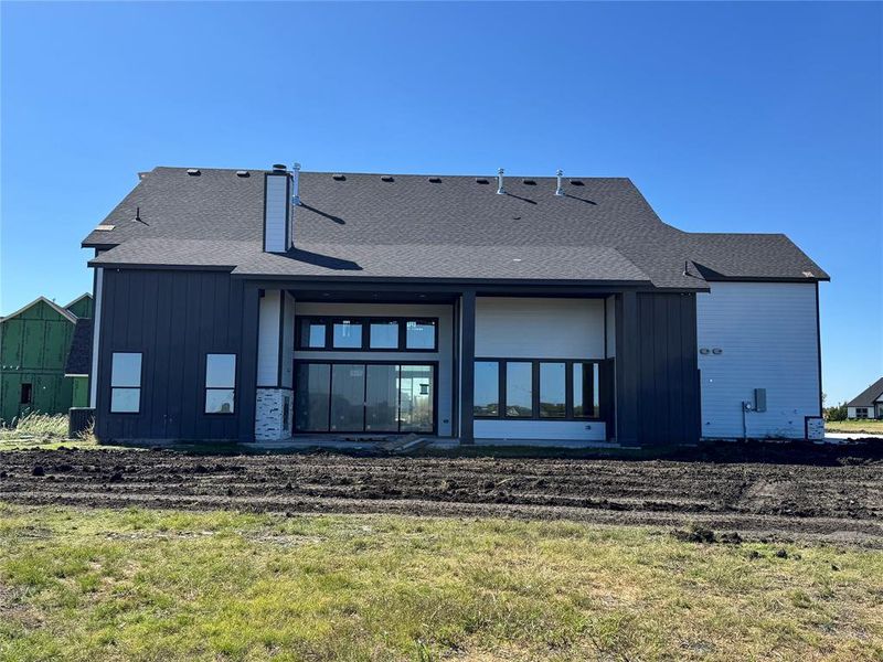 Rear view of property with a patio, roof with shingles, board and batten siding, and a yard