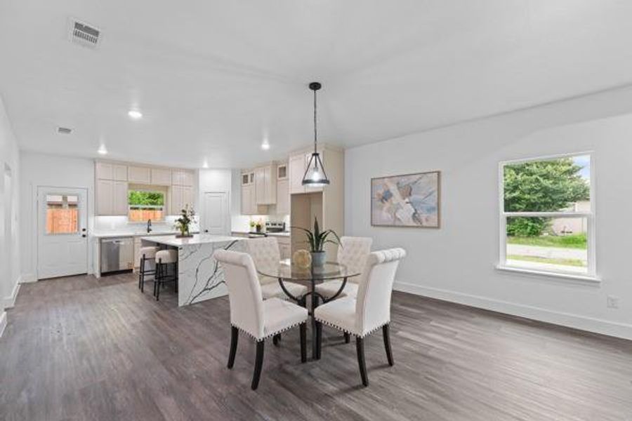 Open-concept living space featuring wood-finish flooring, a kitchen island with stone waterfall countertop, recessed lighting, and a modern pendant fixture Open-concept living space featuring wood-finish flooring, a kitchen island with stone waterfall countertop, recessed lighting, and a modern pendant fixture
