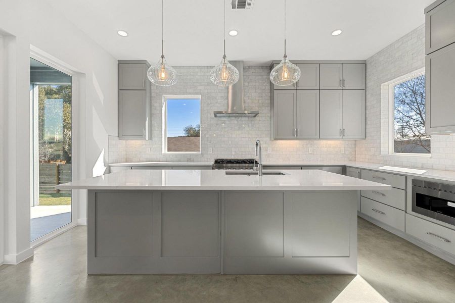 Kitchen with concrete floors, a sink, range hood, gray cabinets, and stainless steel microwave