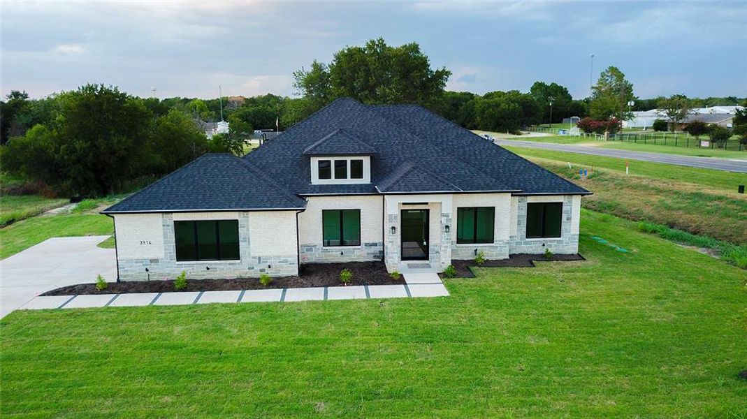 View of front of property with a shingled roof, a front lawn, stone siding, and brick siding