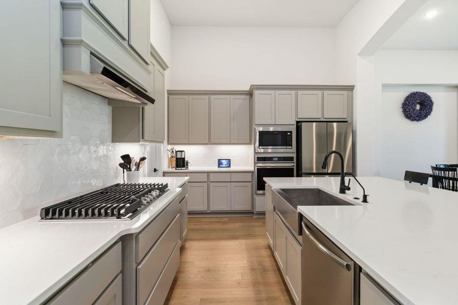 A well-appointed kitchen features stainless steel appliances, pristine white countertops, and light wood flooring.