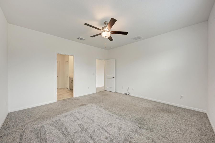 A spacious bedroom featuring soft carpeting and an overhead ceiling fan.