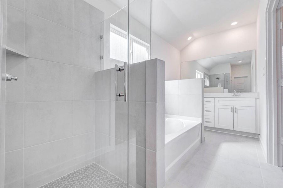 Primary bath view highlighting the glass-enclosed walk-in shower, soaking tub, dual-sink vanity, neutral tile flooring, and bright natural light. The separation between the tub and shower adds comfort and function, while the clean finishes give the space a fresh, spa-inspired look.