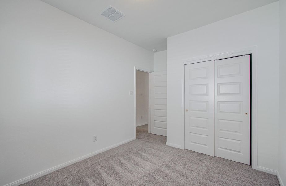 A bright and airy bedroom featuring plush carpet, neutral walls, and a convenient double-door closet for ample storage.