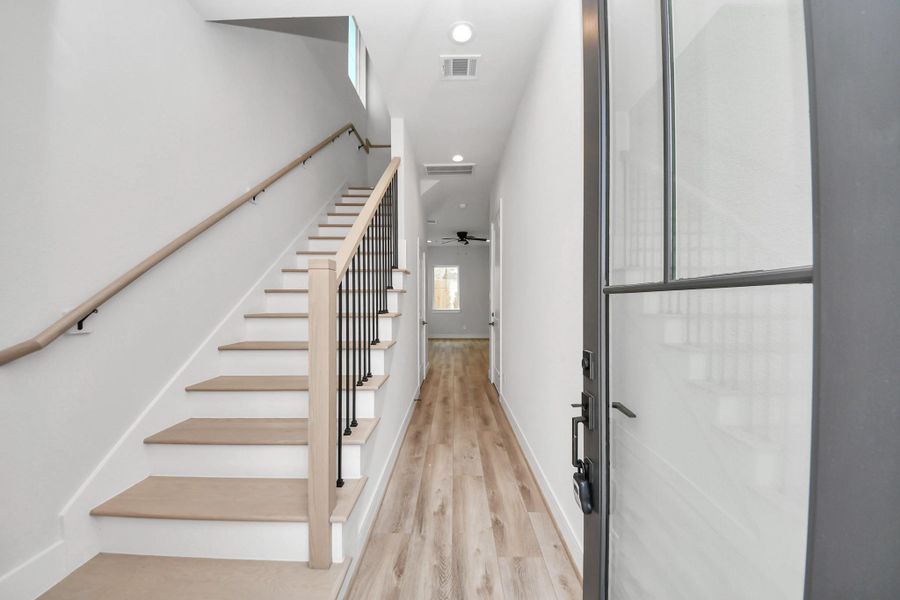 Greeted by elegant glass door, luxury vinyl plank floors, white oak stair case, and long entry way to the living space.
