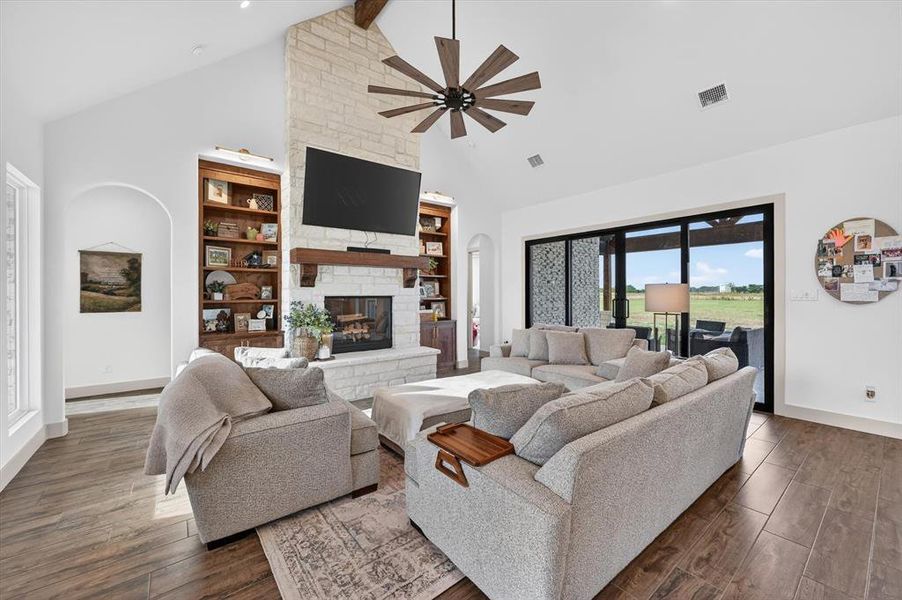 Spacious living area featuring a vaulted ceiling with exposed wood beams, a stone-clad fireplace with a wood mantel, and built-in shelving