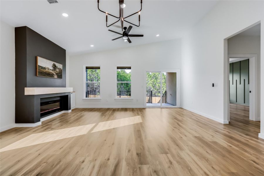 Unfurnished living room featuring a chandelier, plenty of natural light, a glass covered fireplace, light wood-style flooring, and vaulted ceiling Unfurnished living room featuring a chandelier, plenty of natural light, a glass covered fireplace, light wood-style flooring, and vaulted ceiling