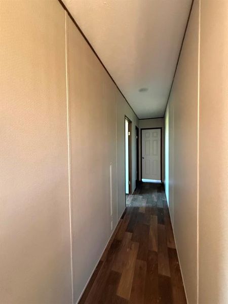 Hallway featuring wood-finish flooring, light-toned walls with vertical paneling, and a white paneled door Hallway featuring wood-finish flooring, light-toned walls with vertical paneling, and a white paneled door