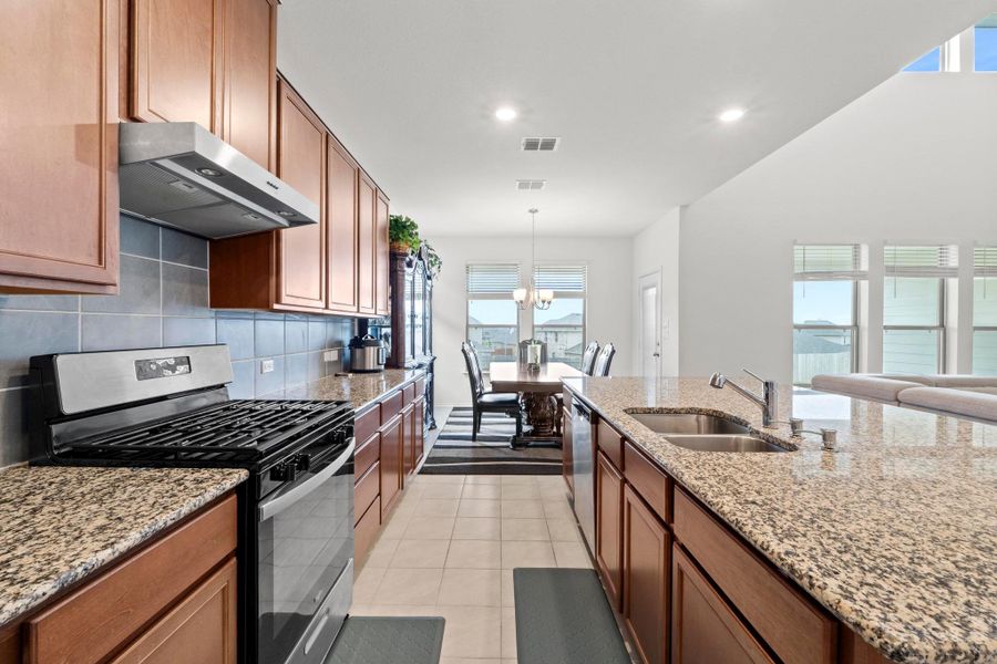 Expansive kitchen featuring wood cabinetry, granite countertops, stainless steel appliances, a tile backsplash, and a double basin sink