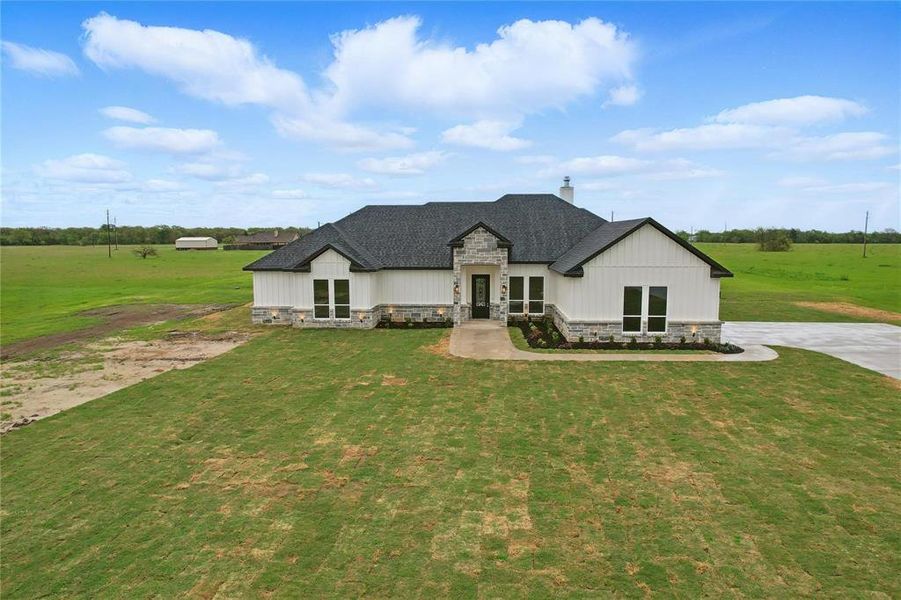 View of front of house with stone siding, a chimney, a front yard, a view of rural / pastoral area, and roof with shingles View of front of house with stone siding, a chimney, a front yard, a view of rural / pastoral area, and roof with shingles