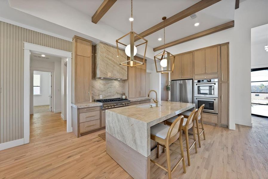 Kitchen with a kitchen breakfast bar, beamed ceiling, appliances with stainless steel finishes, custom exhaust hood, and a center island with sink
