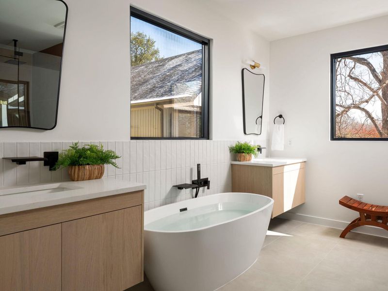 Full bath with two vanities, a freestanding tub, tile walls, and light tile patterned flooring