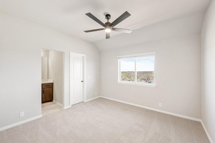 Bedroom with vaulted ceiling, ceiling fan, carpet flooring, and attached bathroom with dark wood vanity
