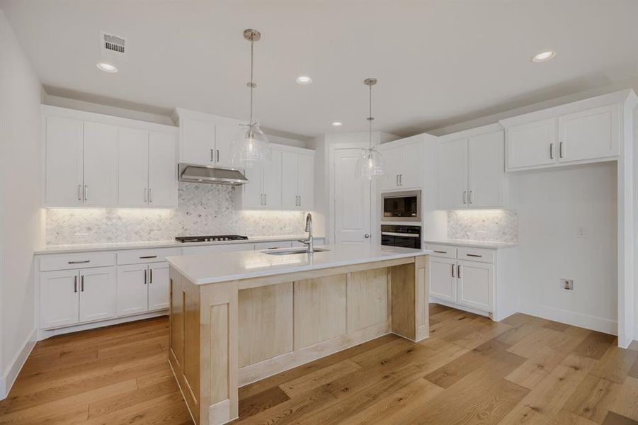 Bright kitchen featuring a light wood-finish island, white cabinetry, integrated stainless steel appliances, and wood-finish flooring