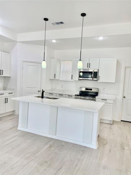 Kitchen with hanging light fixtures, white cabinetry, a kitchen island with sink, light stone countertops, and stainless steel appliances