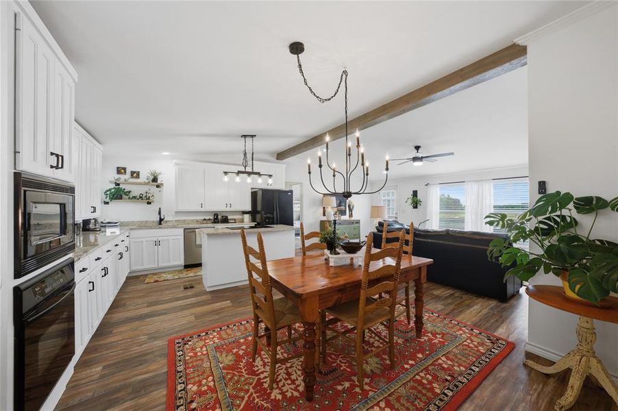 Open-concept kitchen and dining area featuring wood-finish flooring, white cabinetry with black hardware, and an island with a breakfast bar