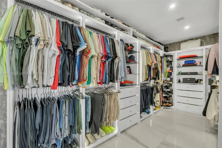 Custom walk-in closet featuring extensive white built-in cabinetry, integrated LED vertical lighting, multiple drawers, open shelving, and polished stone-finish floor tiling Custom walk-in closet featuring extensive white built-in cabinetry, integrated LED vertical lighting, multiple drawers, open shelving, and polished stone-finish floor tiling