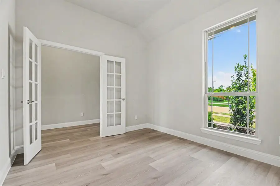 Room featuring French doors with glass panes, wood-finish flooring, a tall window, and white baseboards Room featuring French doors with glass panes, wood-finish flooring, a tall window, and white baseboards