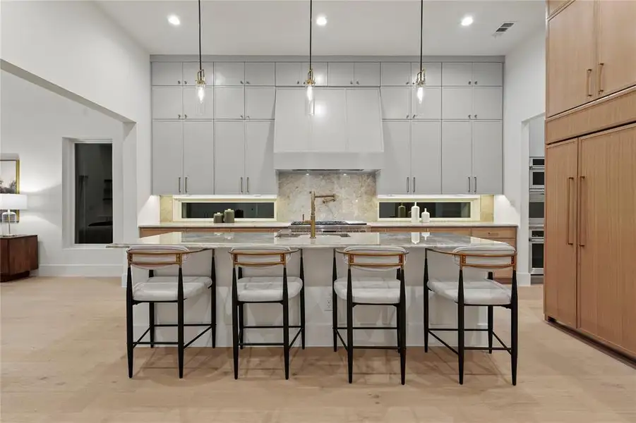 Kitchen with decorative backsplash, a kitchen bar, hanging light fixtures, light stone countertops, and a kitchen island with sink