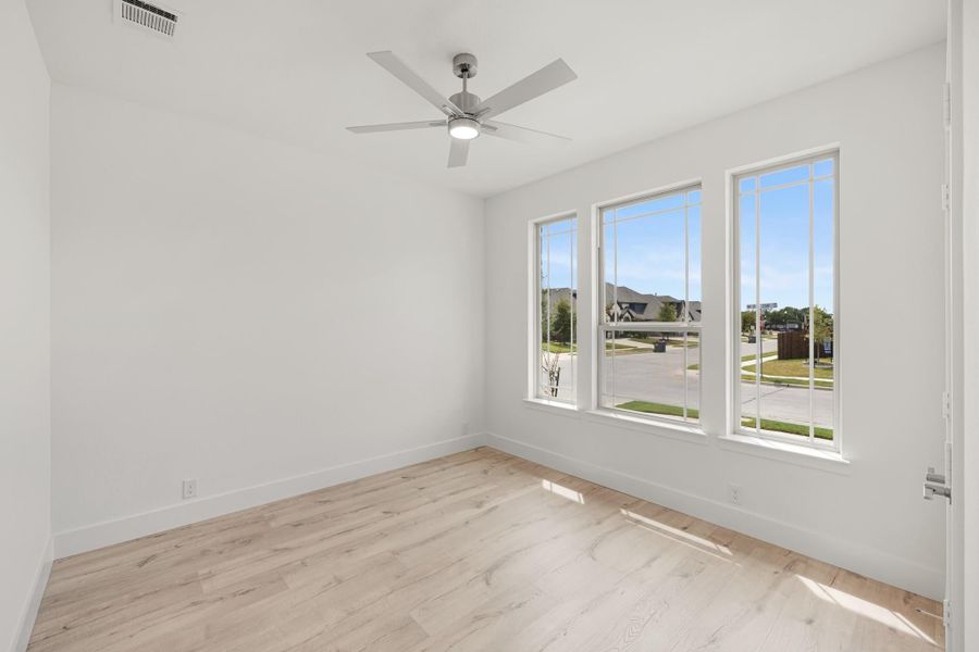 Empty room with light wood floors, ceiling fan, and three large windows with neighborhood views