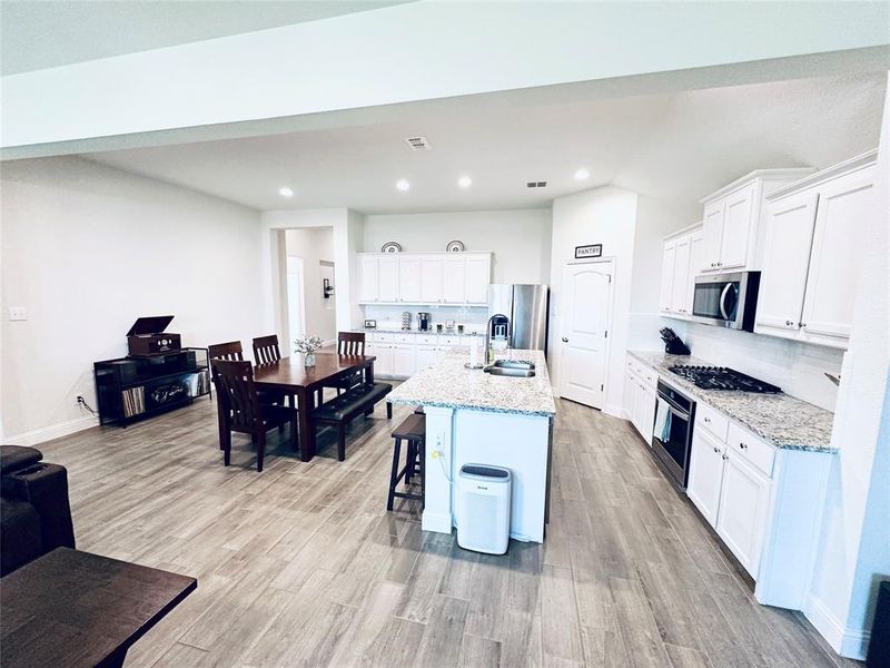 Kitchen featuring appliances with stainless steel finishes, an island with sink, light stone countertops, and light wood-type flooring