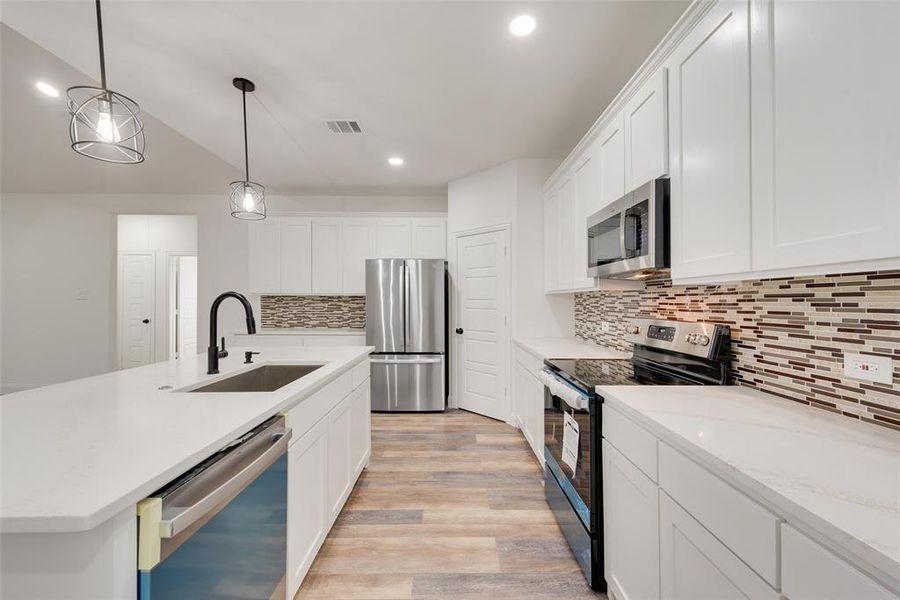 Kitchen with sink, stainless steel appliances, decorative light fixtures, white cabinets, and light hardwood / wood-style flooring