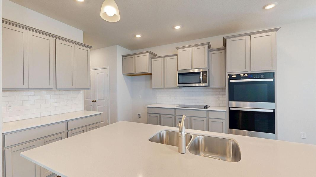 The kitchen features light-colored cabinetry, stainless steel appliances including a microwave and double oven, a white tile backsplash, and recessed lighting